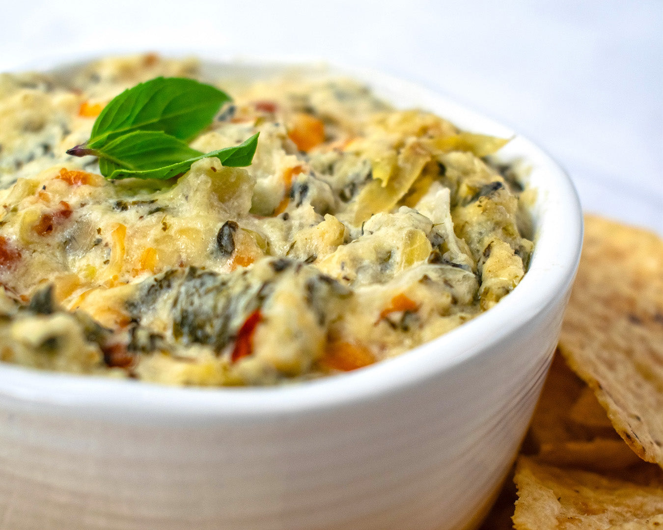 Spinach artichoke dip in a white bowl with tortilla chips on a white background The Signature All Purpose Seasoning